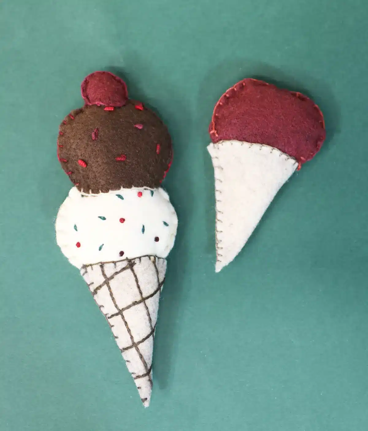 Two charming felt ice cream cone crafts on a green background, perfect for kids to make and sell. The left cone features chocolate and vanilla scoops adorned with sprinkles, while the right showcases a delightful single pink scoop. Ideal projects for budding young entrepreneurs.