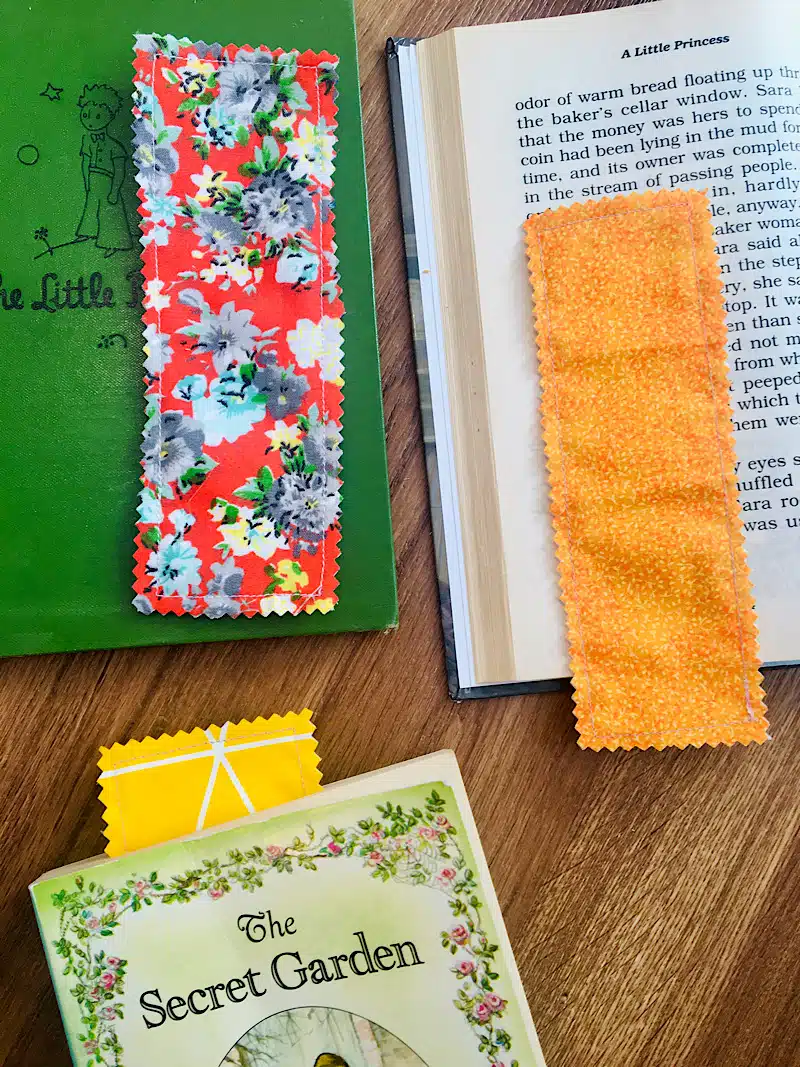 Three fabric bookmarks, perfect crafts for kids to make and sell, are placed on and in books, including