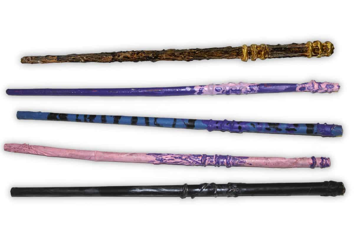 Five decorative wands, perfect for crafts for kids to make and sell, are displayed horizontally. Each features unique designs and colors, showcasing brown, multiple shades of purple, pink, and black.