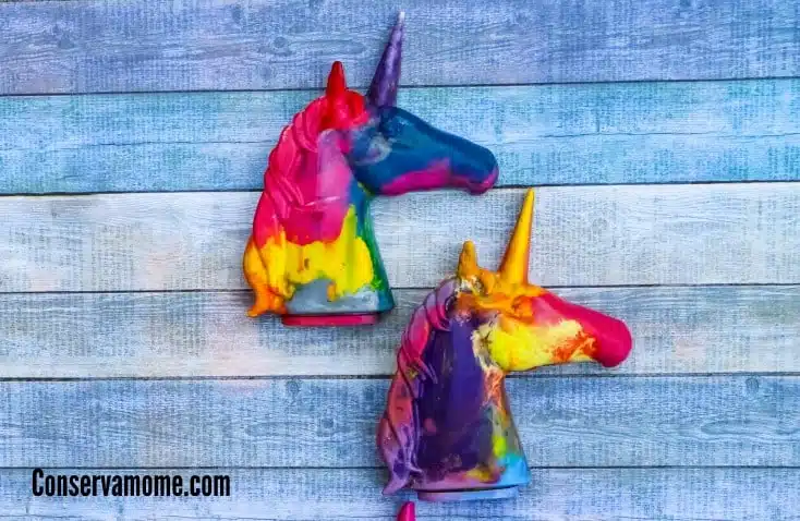 Two colorful wax unicorn heads rest on a wooden surface, showcasing a delightful craft for kids to make and sell.